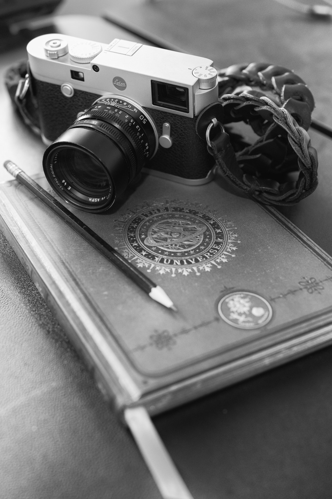 Silver Leica M10-R with a 50mm Summilux and braided leather strap resting on a notebook, a sharpened pencil beside it